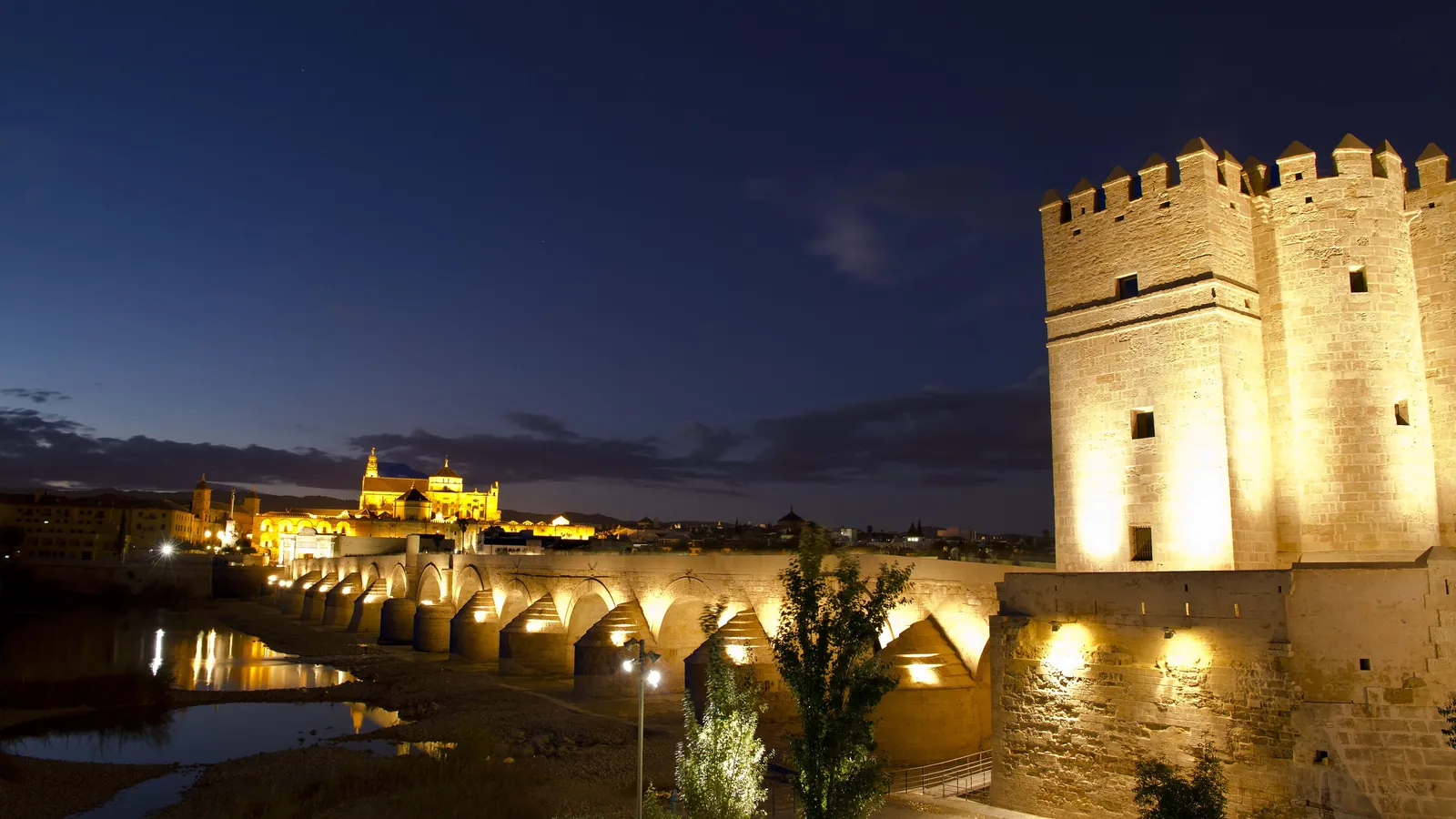 The Calahorra tower, the Roman bridge over the Guadalquivir and the lit Mosque-Cathedral in the distance under a deep blue evening sky