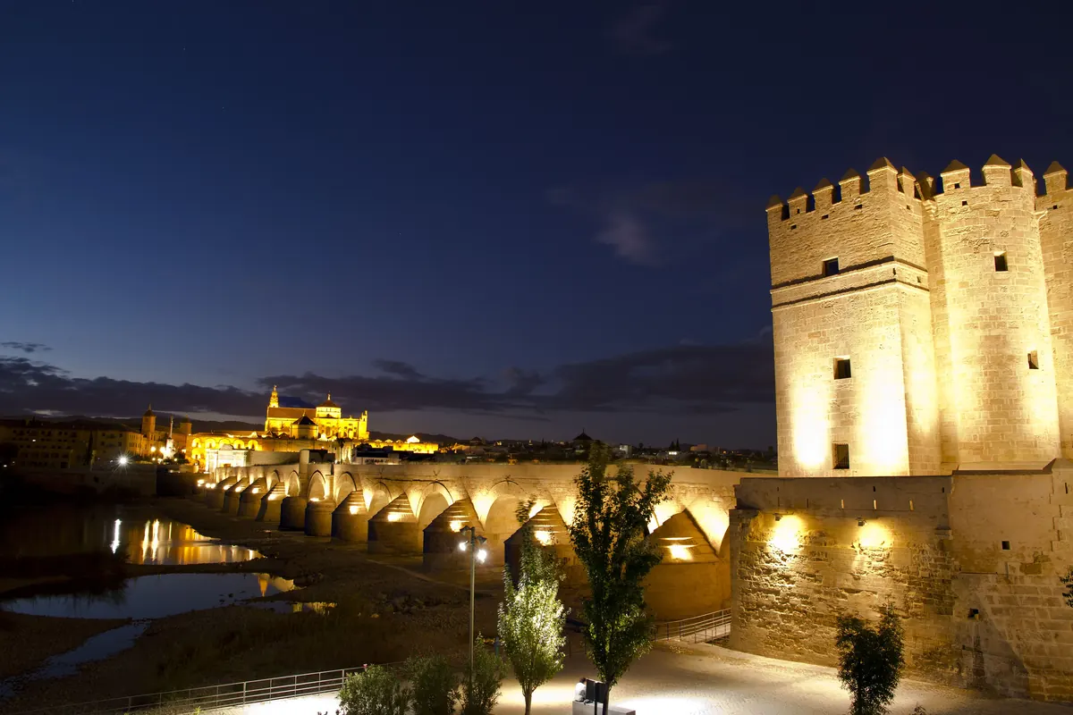 The Calahorra tower, the Roman bridge over the Guadalquivir and the lit Mosque-Cathedral in the distance under a deep blue evening sky